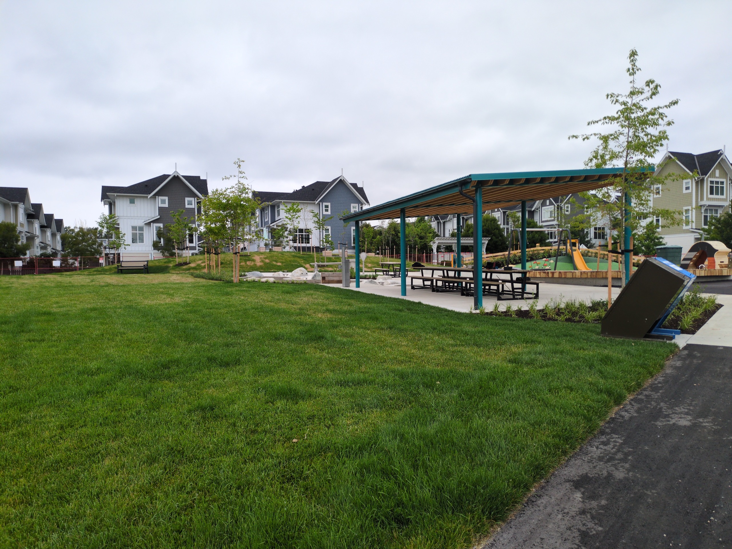 Open lawn behind picnic shelter and plaza in centre of park