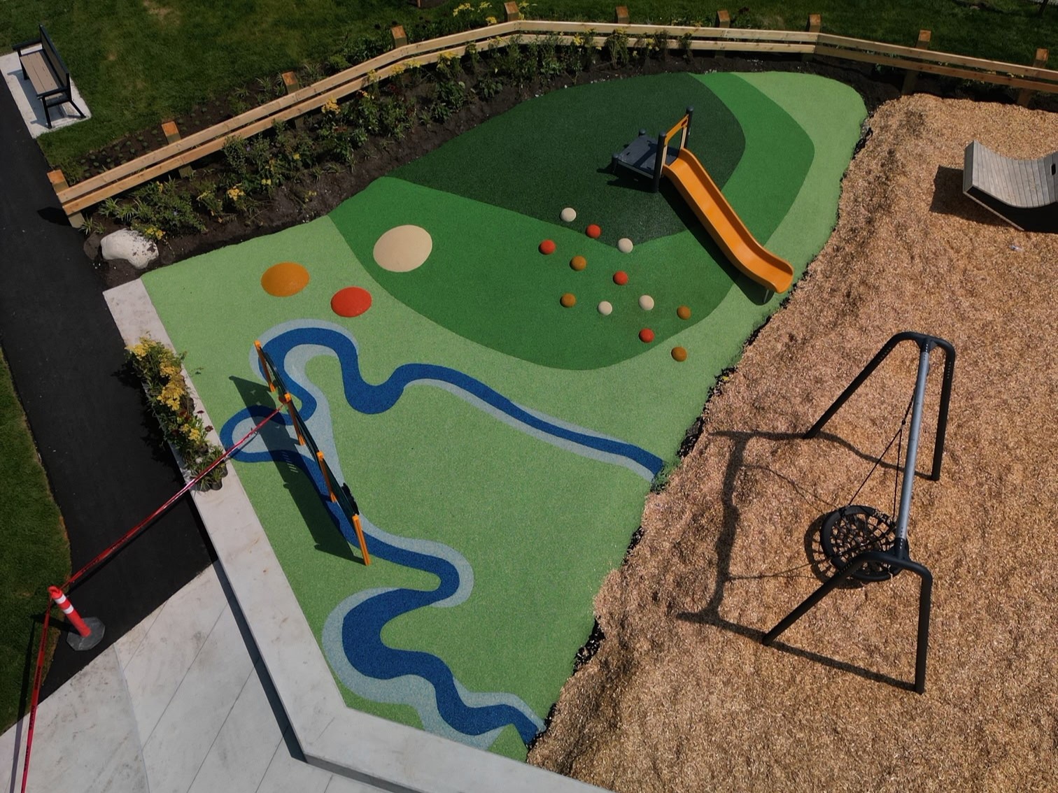 Aerial view of junior play area with yellow hill slide, green rubber, and disc swing on wood chips