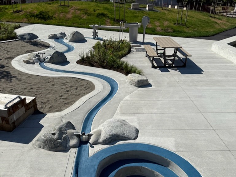 Blue concrete runnel winding from a metal elevated water-play table next to a sandbox
